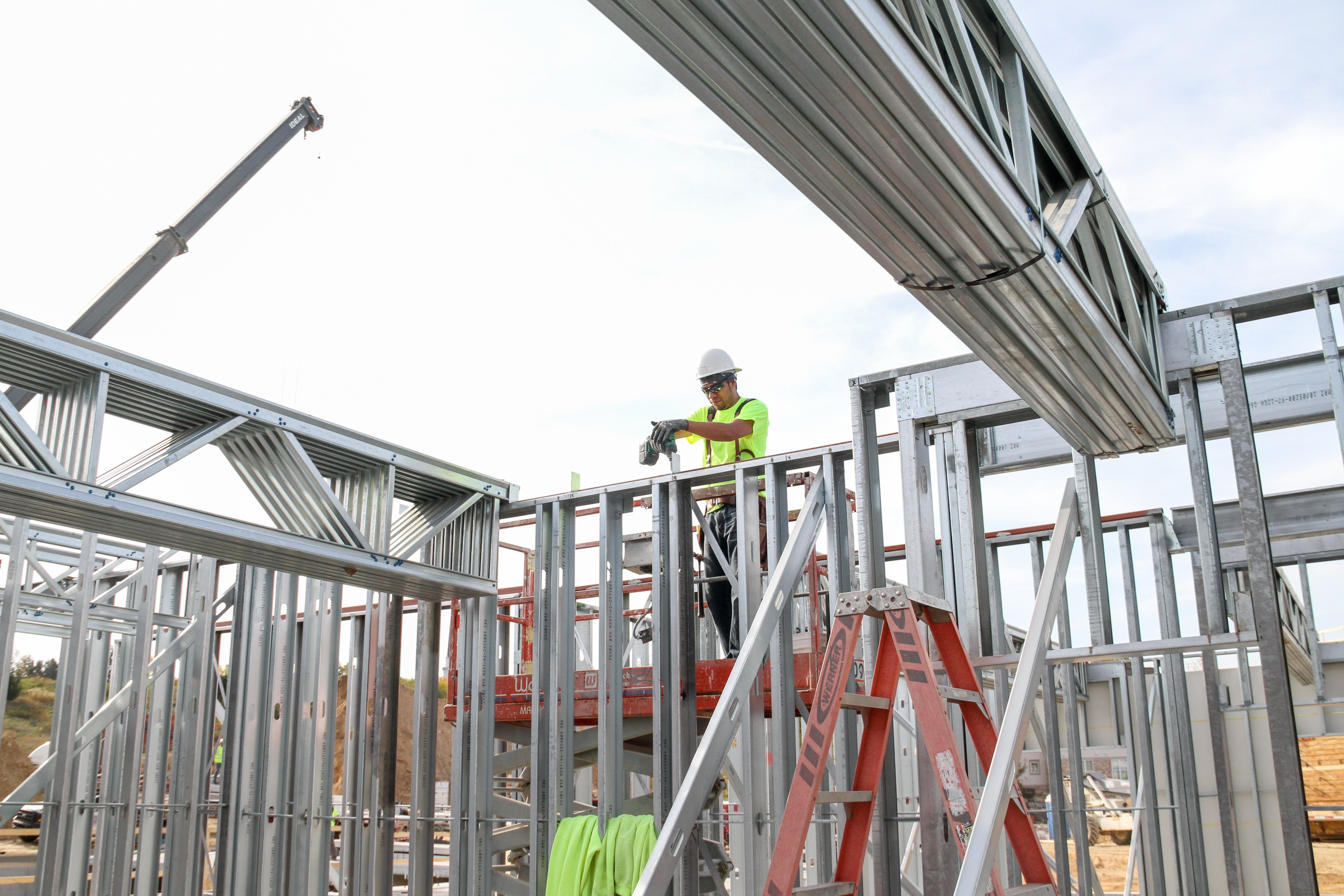 Worker on a lift installing cold-formed steel wall panel framing on a mid-rise job site.